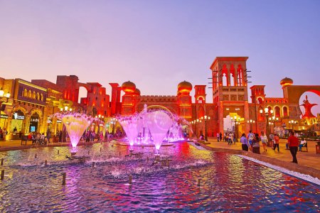 Foto de DUBAI, Emiratos Árabes Unidos - 6 de marzo de 2020: Las coloridas fuentes de baile en la Plaza de la Cultura de Global Village Dubai, la Puerta Cultural con cazadores de viento y cúpulas de cebolla se ve en el fondo, el 6 de marzo en Dubai - Imagen libre de derechos