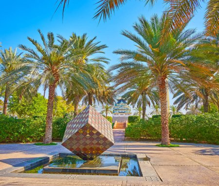 Photo for The small fountain with sculpture of balancing cube, surrounded with palms and lush bushes of Zabeel Park, Dubai, UAE - Royalty Free Image