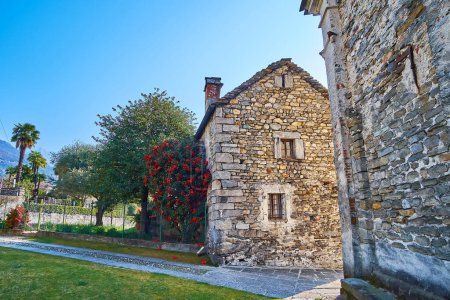 Téléchargez les photos : La petite maison du prêtre à l'église San Quirico avec un buisson luxuriant de camélia dans le jardin, Locarno, Suisse - en image libre de droit
