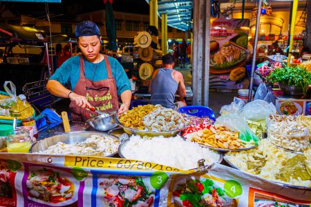 Photo for BANGKOK, THAILAND - APRIL 23, 2019: The young vendor of Khaosan road night market cooks traditional Thai dishes with steamed seafood, fish, noodles, vegetables, herbs and spices, on April 23 in Bangkok - Royalty Free Image