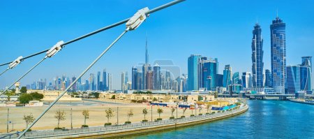Téléchargez les photos : DUBAI, Émirats arabes unis - 6 MARS 2020 : Paysage urbain panoramique avec horizon futuriste derrière le canal d'eau de Dubaï avec des câbles du pont Safa au premier plan, le 6 mars à Dubaï - en image libre de droit