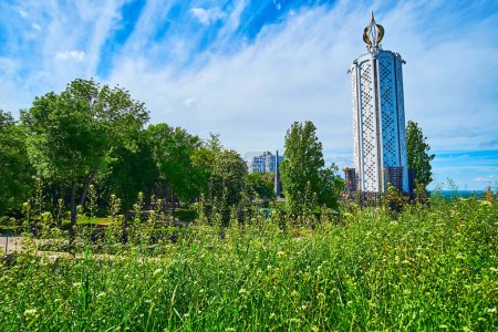 Téléchargez les photos : Les herbes vertes luxuriantes et les fleurs sauvages devant le monument de l'Holodomor de la Bougie de la Mémoire (Grande Famine) en arrière-plan, Kiev, Ukraine - en image libre de droit