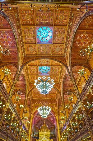 Foto de BUDAPEST, HUNGRÍA - 22 DE FEB DE 2022: El techo ricamente decorado de la sinagoga de Dohany Street con patrones geométricos tradicionales, vidrieras y lámparas de araña, el 22 de febrero en Budapest - Imagen libre de derechos