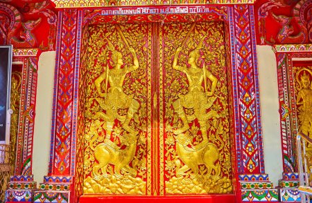 Photo for The carved wooden red doors of the Viharn of Wat Khuan Khama temple, decorated with gilt ornaments and sculptures, Chiang Mai, Thailand - Royalty Free Image