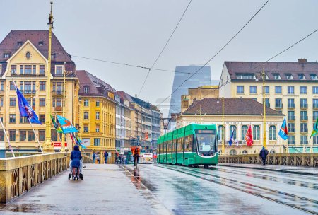 Téléchargez les photos : BASEL, SWITZERLAND - APRIL 1, 2022: The view on modern green tram ridding on Mittlere Brucke on rainy day, on April 1 in Basel, Switzerland - en image libre de droit