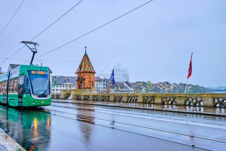Photo for BASEL, SWITZERLAND - APRIL 1, 2022: The green tram rides on Mittlere Brucke with Kappelijoch chapel on background, on April 1 in Basel, Switzerland - Royalty Free Image