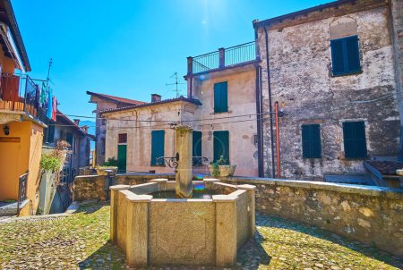 Fontaine médiévale en pierre et logement historique sur la Piazza Rusciett, Castello, Valsolda, Italie
