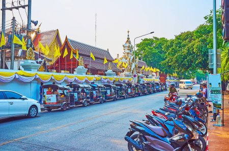 Téléchargez les photos : CHIANG MAI, THAÏLANDE - 3 MAI 2019 : Prapokkloa Road avec tuk tuk et parking vélo et clôture sculptée de Wat Chedi Luang, décorée de drapeaux jaunes, Chiang Mai - en image libre de droit
