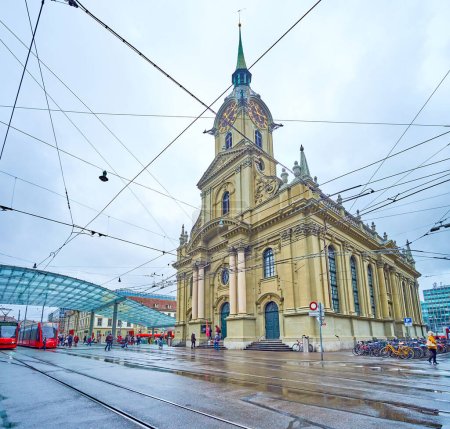 Foto de BERN, SUIZA - 31 DE MARZO DE 2022: Escena urbana en Bubenbergplatz con estación de tranvía bajo dosel de cristal moderno y Heiliggeistkirche histórico, el 31 de marzo en Berna, Suiza - Imagen libre de derechos
