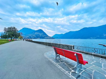 Photo for Pedestrian promenade on Lake Lugano with bright red benches, spread trees and Monte Bre in background, Lugano, Switzerland - Royalty Free Image