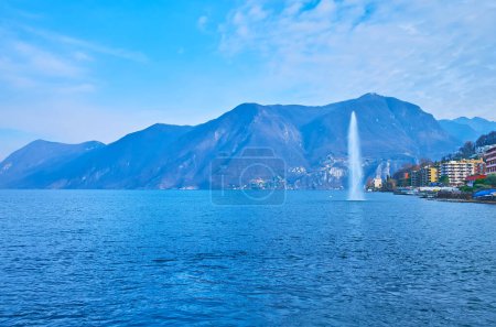 Photo for The mountain landscape behind the blue Lake Lugano and Water Jet of Paradiso fountain in background, Lugano, Switzerland - Royalty Free Image