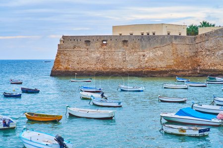 Téléchargez les photos : Le bastion médiéval en pierre du château de Santa Catalina avec de petits bateaux de pêche au premier plan, Cadix, Espagne - en image libre de droit