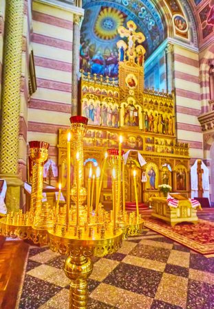 Photo for CHERNIVTSI, UKRAINE - JULY 16, 2021: The gilt candle holder with burning candles against the iconostasis in Seminary Church of Chernivtsi National University, on July 16 in Chernivtsi - Royalty Free Image