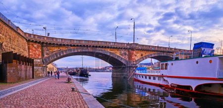 Foto de El viejo puente de piedra Palacky con barco turístico, amarrado en la orilla de Naplavka Embankment, Praga, Chequia - Imagen libre de derechos