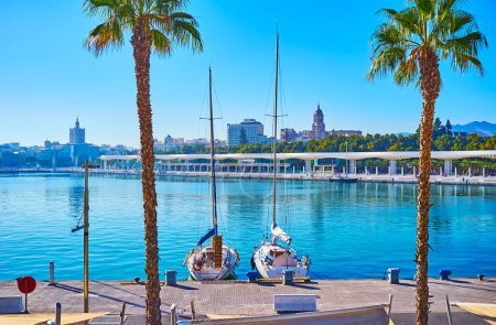 Téléchargez les photos : Deux petits voiliers amarrés dans le port de Malaga contre la Palmeraie des Surprises ruelle et parc vert de la ville, Espagne - en image libre de droit