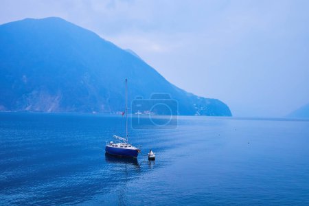 El pequeño barco solitario está atado a la boya en el lago Lugano, Lugano, Suiza