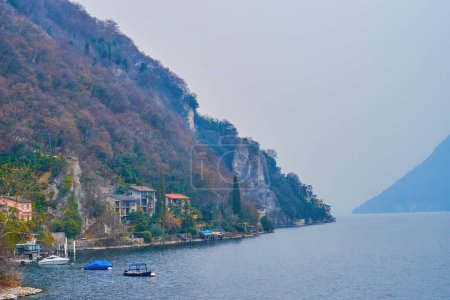 The rocky shore of Lake Lugano with tied up boats, Lugano, Switzerland