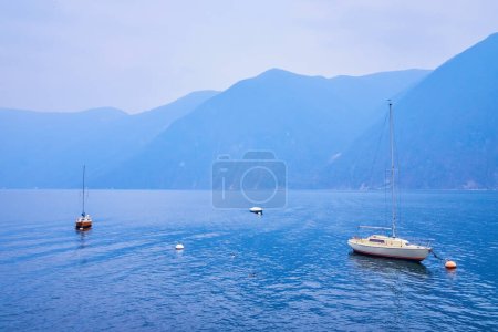 The small yachts are tied up to the buoys in  Lugano Lake, Lugano, Switzerland