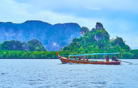 Traditional wooden longtail boat floats along the mangroves and rocks, Phang Nga Bay, Thailand