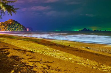 Téléchargez les photos : Promenade nocturne romantique le long de la plage de sable avec vue sur les îles rocheuses à l'horizon et lumières vives de bateaux de tourisme, Ao Nang, Krabi, Thaïlande - en image libre de droit