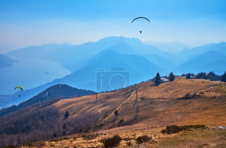 The sunny hazy day on Cimetta Mount with a view of the glider aircrafts, flying over the mountain slopes, Ticino, Switzerland