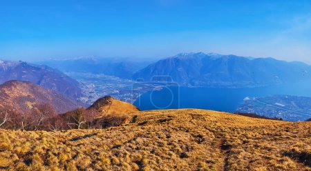 Panorama of Cimetta mountain slope with a footpath to Alpe Cardada, seen against the valley with Lake Maggiore, Locarno, Monte Tamaro and Monte Gambarogno, Ticino, Switzerland