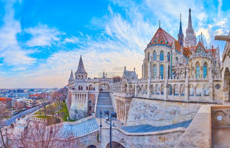 Panorama of the carved Fisherman's Bastion with staircases, arched galleries and towers with ornate Matthias Church in background, Budapest, Hungary