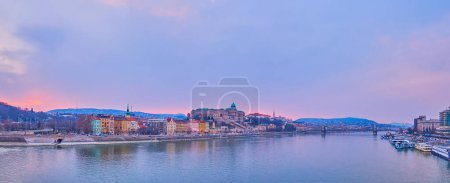 Panorama of Budapest with bright dusk sky, reflected on Danube waters, Taban neighborhood houses and Buda Castle atop the hill, Budapest, Hungary