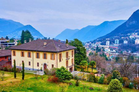 Altes Wohnhaus in den Gärten der St. Abundius-Anlage, im Hintergrund alpine Berge, Collina d 'Oro, Schweiz