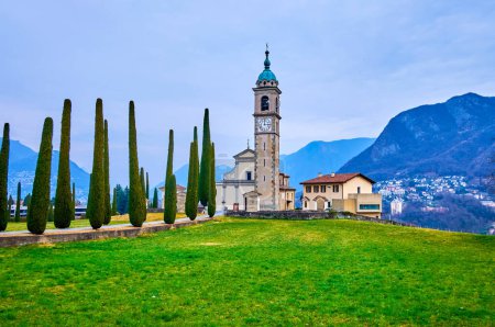 Césped verde y cipreses altos en el parque de la iglesia de San Abundio (Sant 'Abbondio), Collina d' Oro, Ticino, Suiza