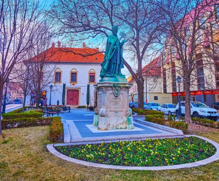 The bronze statue of Pope Innocent XI in the small park with flower beds on Hess Andras Square, Buda Castle Quarter, Budapest, Hungary