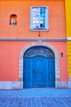 Die Fassade des alten Wohnhauses in der Tancsics Mihaly Straße im Budaer Burgviertel, dekoriert mit einer gewölbten Holztür und einem steinernen mittelalterlichen Königskopf in einer kleinen Nische, Budapest, Ungarn