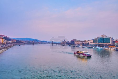 Photo for The evening cityscape with purple waters of Danube, Szechenyi Chain Bridge and the tourist ferry, floating along the old town of Budapest, Hungary - Royalty Free Image