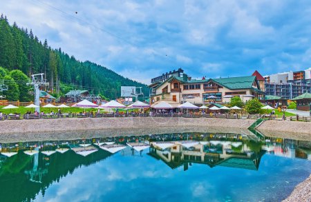 Photo for The mirror-like Trout Pond with restaurants and hotels in the background, Bukovel, Carpathians, Ukraine - Royalty Free Image