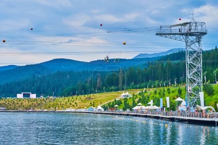 Téléchargez les photos : Les touristes apprécient la tyrolienne tour à vélo sur le lac Molodiste, Bukovel, Carpates, Ukraine - en image libre de droit