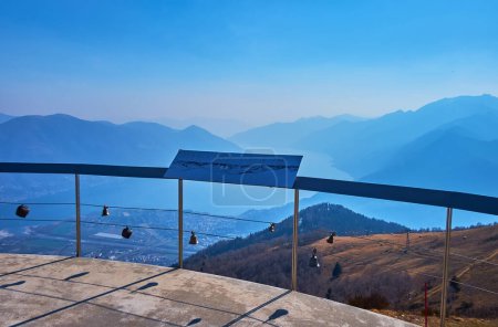Die Aussichtsterrasse auf dem Gipfel der Cardada Cimetta mit kleinen Glocken am Zaun und atemberaubender Aussicht auf die Berge und den Lago Maggiore, Tessin, Schweiz