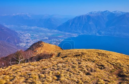 Téléchargez les photos : La pente jaune desséchée de la Cardada Cimetta et l'Alpe Cardada contre la vallée montagneuse brumeuse avec le lac Majeur et les Alpes en arrière-plan, Tessin, Suisse - en image libre de droit