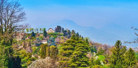 Panoramic mountain landscape from San Vigilio Castle, observing picturesque green Monte Bastia with vintage villas and green gardens, seen behind the trees, Bergamo, Italy