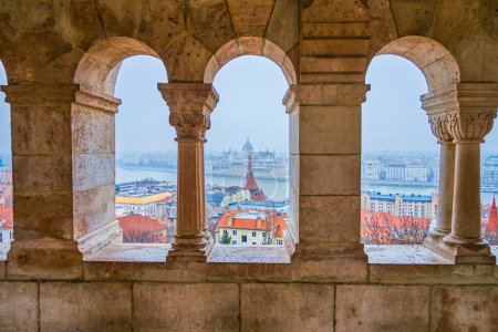 La vue à travers les fenêtres de l'arcade au Bastion des Pêcheurs, mettant en valeur le Parlement, les maisons et le Danube à Budapest, Hongrie.