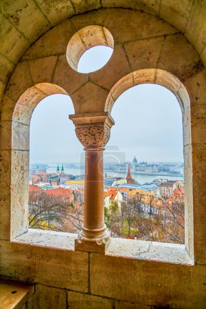 The view through the windows of the arcade at Fisherman's Bastion, showcasing Parliament, houses and the Danube River in Budapest, Hungary.