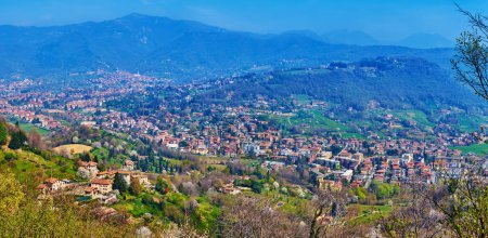 Aussichtsreiche grüne Täler und Berge von der Spitze des Hügels San Vigilio, bewachsen mit hohen grünen Bäumen, Bergamo, Italien