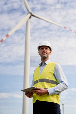 Téléchargez les photos : Ingénieur caucasien tenant tablette numérique et debout sur le champ des éoliennes - en image libre de droit