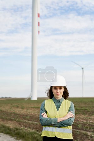 Téléchargez les photos : Portrait d'une ingénieure caucasienne tenant une tablette numérique et debout sur le champ des éoliennes - en image libre de droit