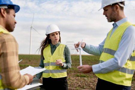 Téléchargez les photos : Équipe d'ingénieurs caucasiens et latins debout sur le terrain des éoliennes et discutant de modèles en plastique - en image libre de droit
