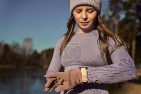 Photo for Caucasian young woman checking parameters on the smartwatch being outdoors in the winter - Royalty Free Image