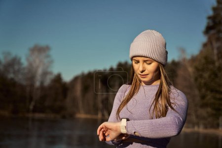 Téléchargez les photos : Caucasienne jeune femme vérifier les paramètres sur la smartwatch être à l'extérieur en hiver - en image libre de droit