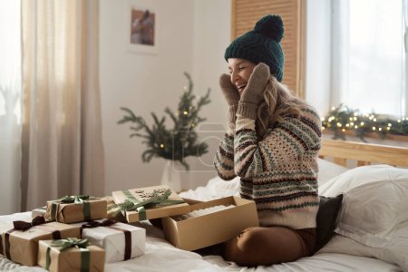 Foto de Mujer caucásica abriendo y probándose regalos de Navidad en su dormitorio - Imagen libre de derechos
