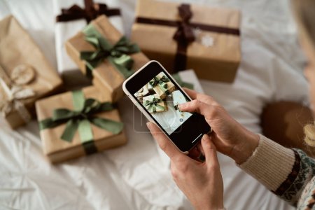 Téléchargez les photos : Mains de femme méconnaissable prenant des photos avec téléphone intelligent de cadeaux de Noël emballés - en image libre de droit