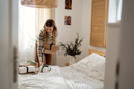 Téléchargez les photos : Femme caucasienne cueillette cadeaux de Noël du lit dans la chambre - en image libre de droit