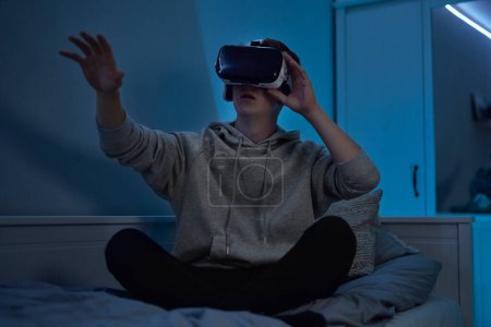 Photo for Teenage caucasian boy using virtual reality glasses while sitting in bedroom at night - Royalty Free Image